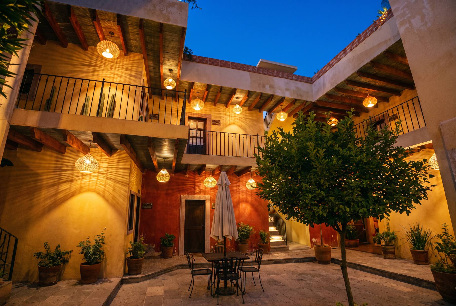 Patio interior de Hotel Bitos al anochecer, con balcones de viga de madera, barandales de herrería y lámparas de mimbre encendidas